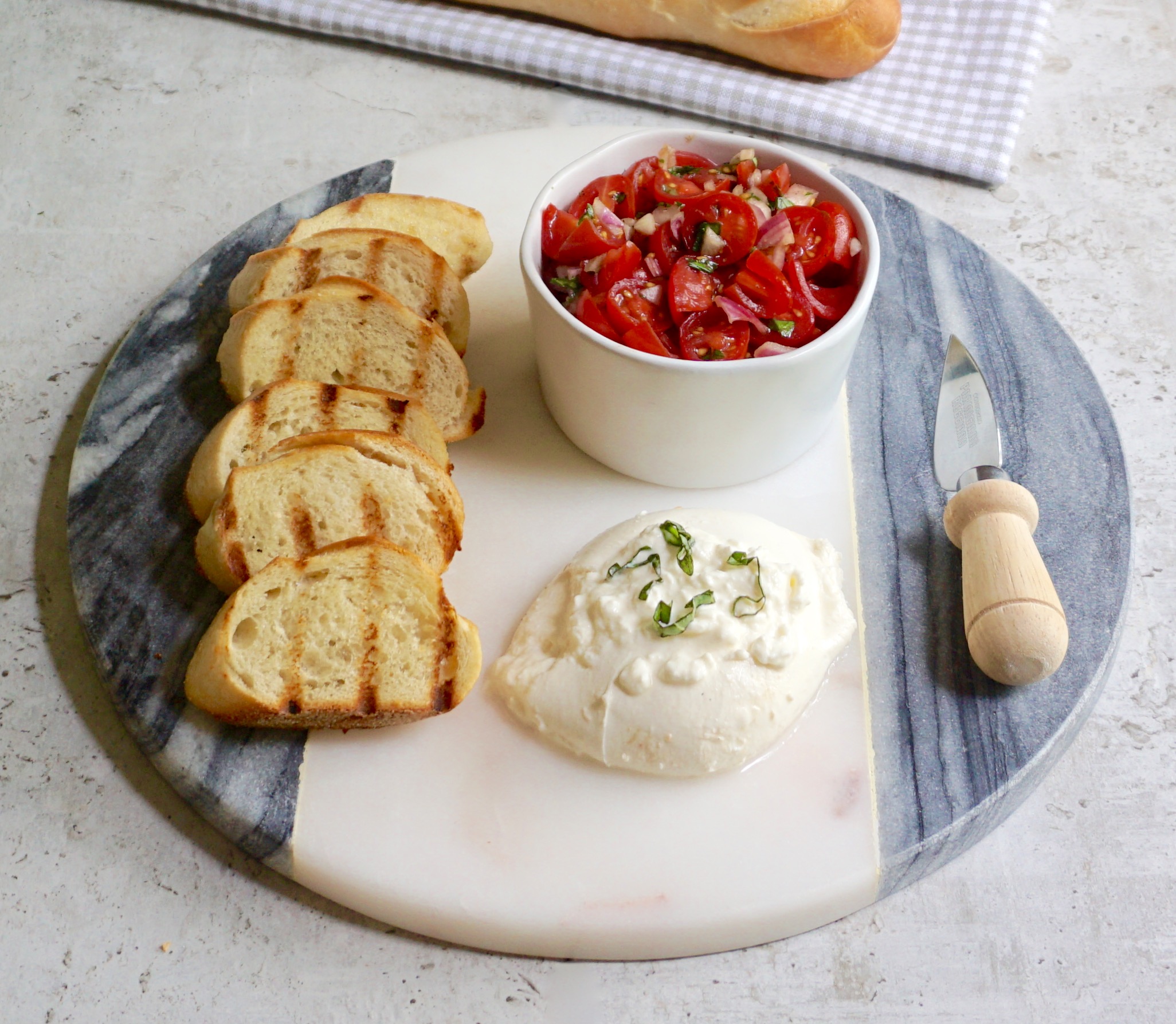 Burrata Bruschetta is a toasted baguette served with burrata tomatoes.