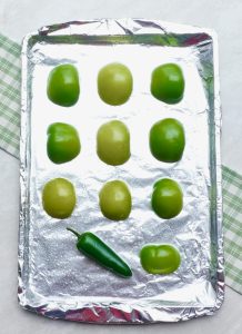Baking sheet with tomatillos and jalapeno pepper.